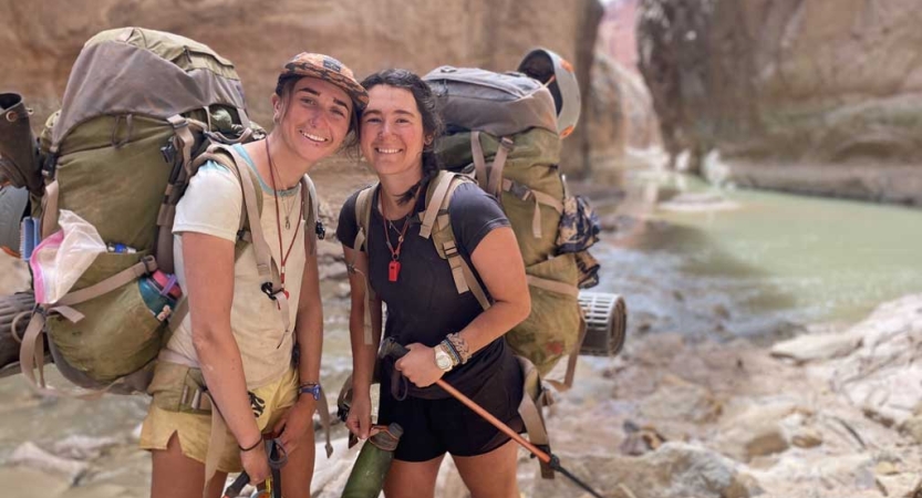 Two people wearing backpacks smile for a photo in a water-filled canyon